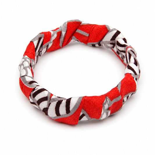 Bracelet jonc ondulé en bois recouvert de tissu wax rouge, blanc et gris aux motifs graphiques noirs, isolé sur fond blanc.
