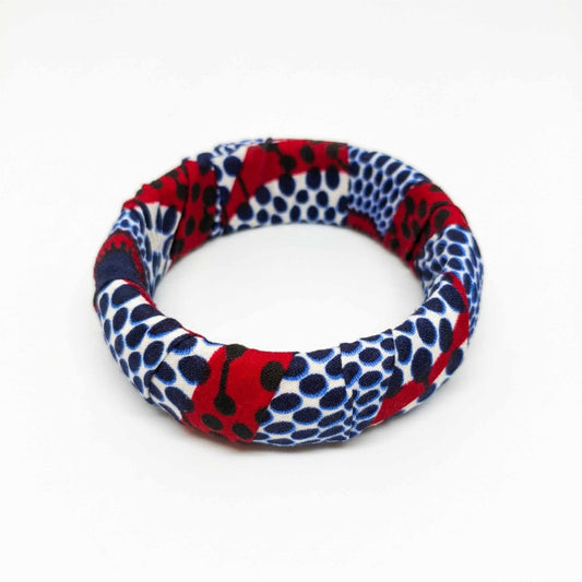 Bracelet jonc rigide en tissu wax rouge vif et bleu marine avec motifs géométriques et pois blancs.