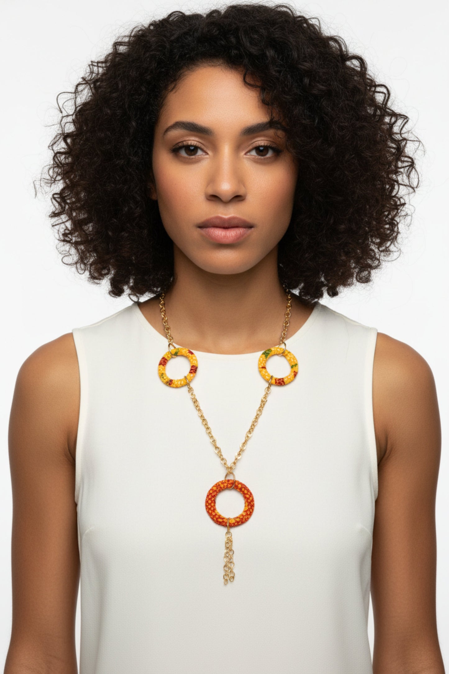Femme portant un collier sautoir doré avec anneaux recouverts de tissu wax jaune orangée et grand anneau central orange rouge avec chaîne pendante - Bijou artisanal africain Djêkoo Wax