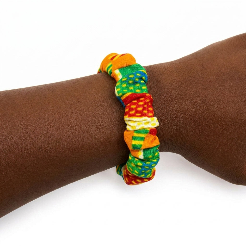 Bracelet en tissu wax africain multicolore (rouge, jaune, vert, bleu) porté au poignet d'une personne à la peau foncée, sur fond blanc