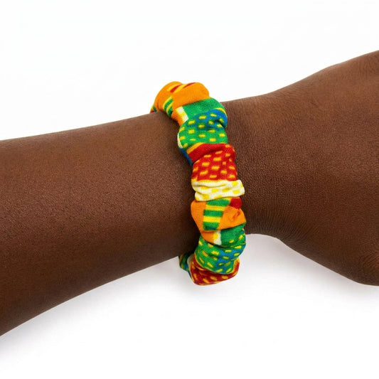 Bracelet en tissu wax africain multicolore (rouge, jaune, vert, bleu) porté au poignet d'une personne à la peau foncée, sur fond blanc
