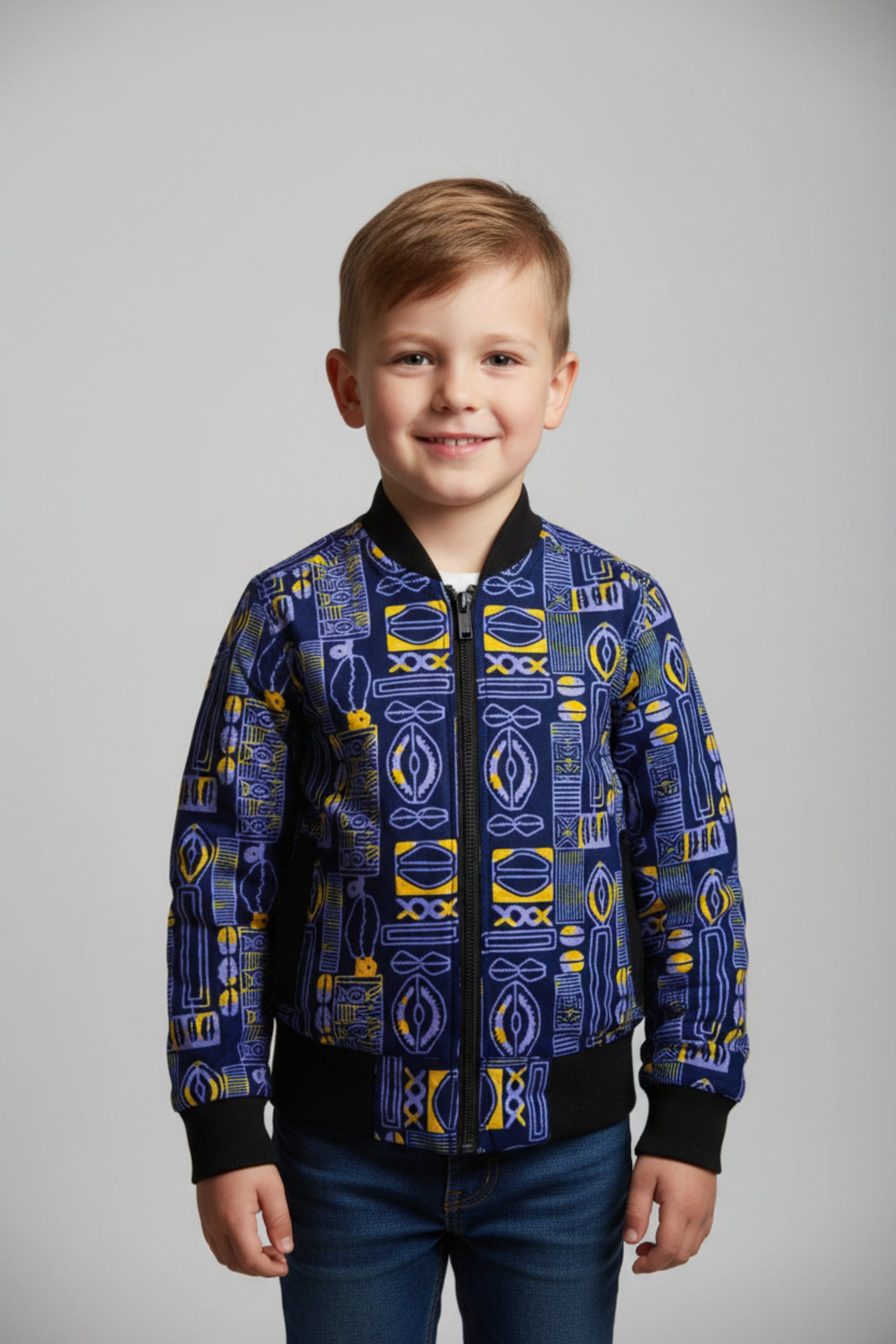 Garçon portant un bomber jacket en tissu wax bleu marine à motifs Adinkra jaune et blanc avec manches et col côtelés noirs et fermeture éclair centrale - Vêtement enfant africain Djêkoo Wax