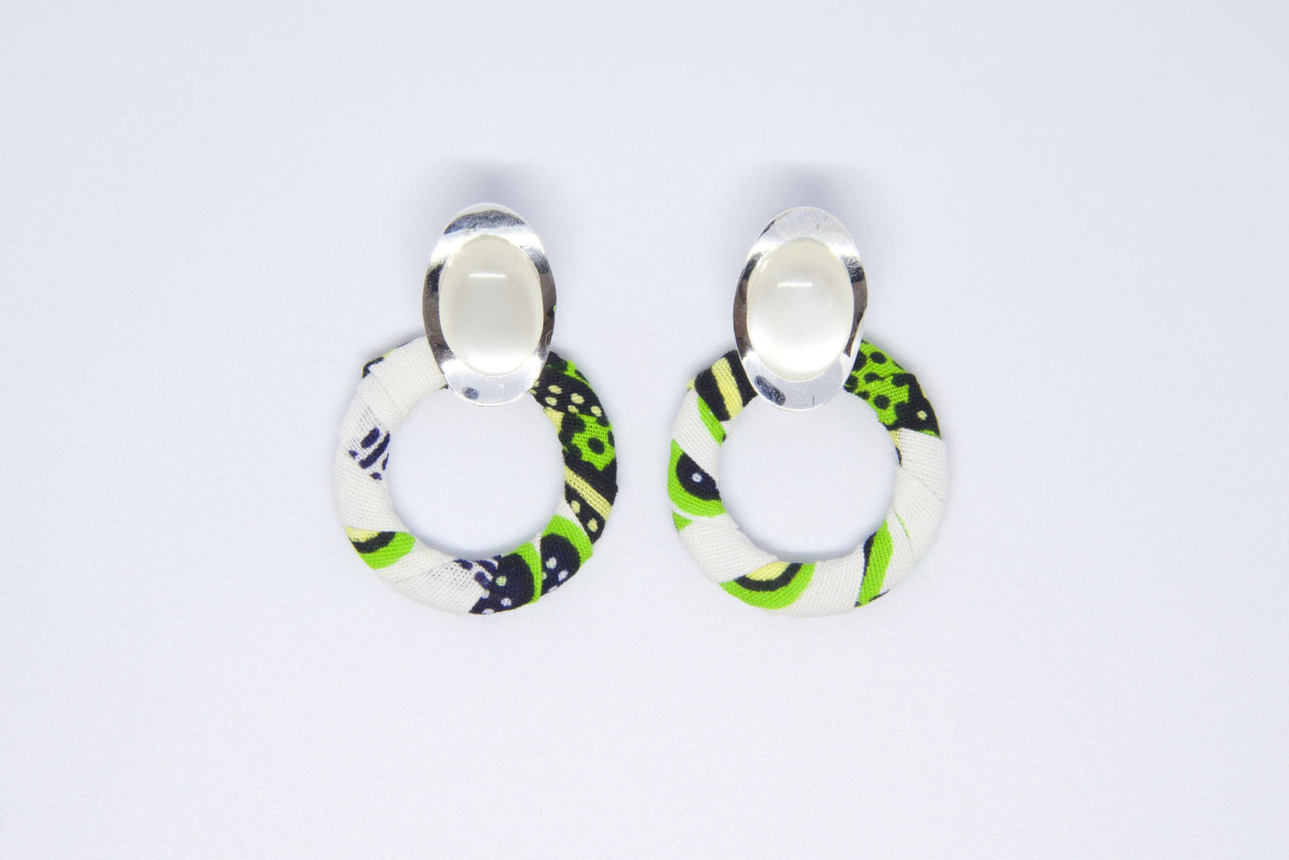 vue face boucles d'oreilles créoles artisanales recouvertes de tissu wax vert anis, noir et blanc avec cabochon ovale argenté - Bijou africain fait main Djêkoo Wax

