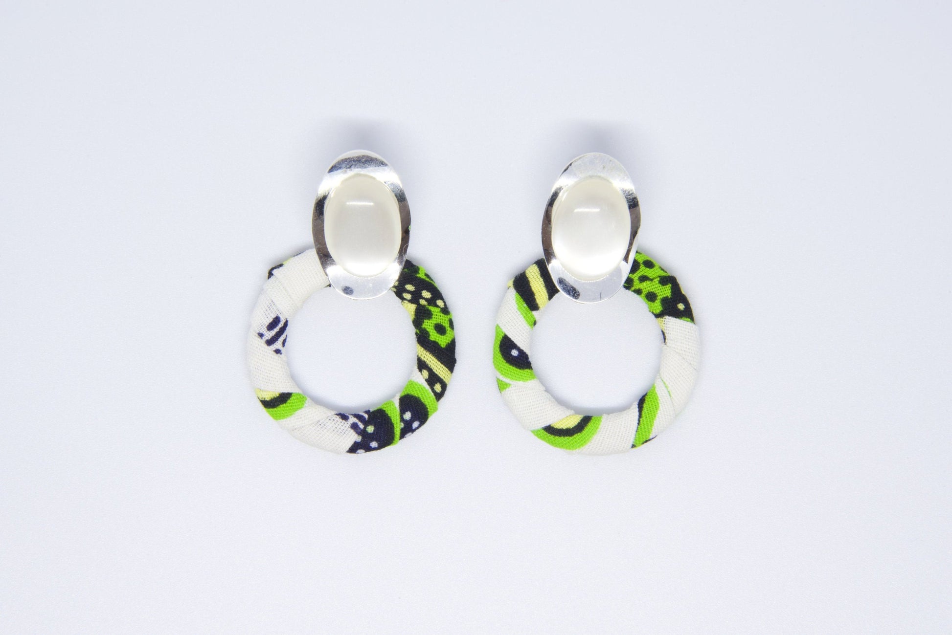 vue face boucles d'oreilles créoles artisanales recouvertes de tissu wax vert anis, noir et blanc avec cabochon ovale argenté - Bijou africain fait main Djêkoo Wax

