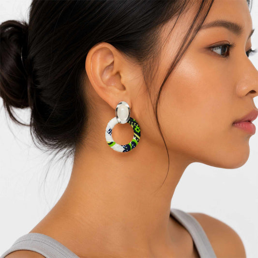 Boucles d'oreilles créoles en tissu wax vert, blanc et noir avec attache argentée portées.