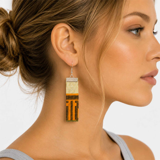 Boucles d'oreilles pendantes en tissu wax orange, noir et beige avec attache argentée, portées.