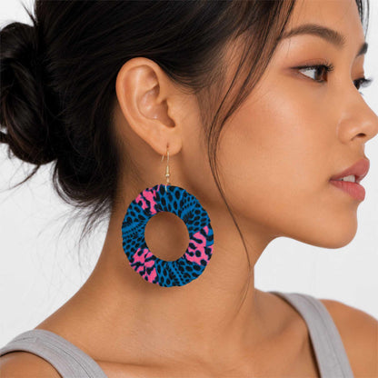 Boucles d'oreilles pendantes artisanales en tissu wax africain, forme cercle ajouré, motif léopard bleu électrique et rose fuchsia à taches noires — portées en situation