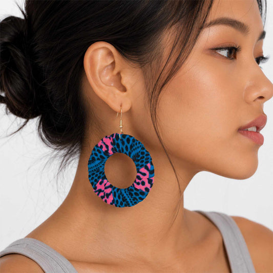 Boucles d'oreilles pendantes artisanales en tissu wax africain, forme cercle ajouré, motif léopard bleu électrique et rose fuchsia à taches noires — portées en situation