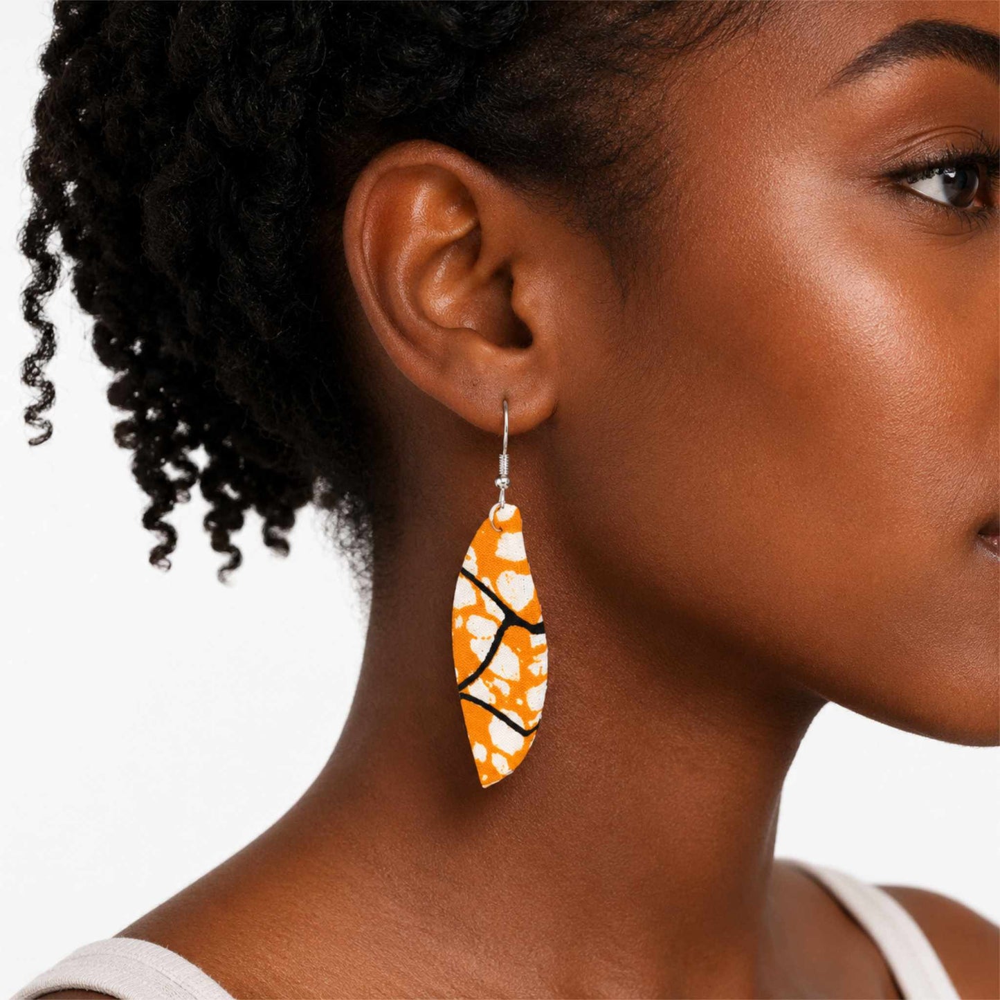 Boucles d'oreilles pendantes artisanales en tissu wax africain, forme feuille, motif graphique orange avec taches blanches et lignes noires — portées en situation