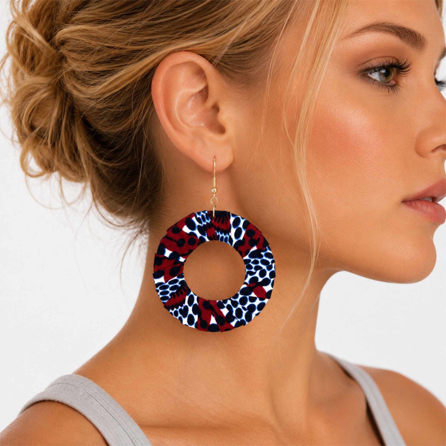 Boucles d'oreilles pendantes artisanales en tissu wax africain, forme cercle ajouré, motif léopard blanc à pois marine et taches bordeaux — portées en situation