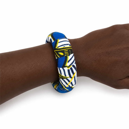 Bracelet africain artisanal large recouvert de tissu wax bleu, blanc, noir et jaune, présenté porté au poignet sur fond blanc.