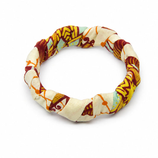 Bracelet jonc ondulé en bois recouvert de tissu wax beige ,bleu, détails jaunes et rouges, isolé sur fond blanc.