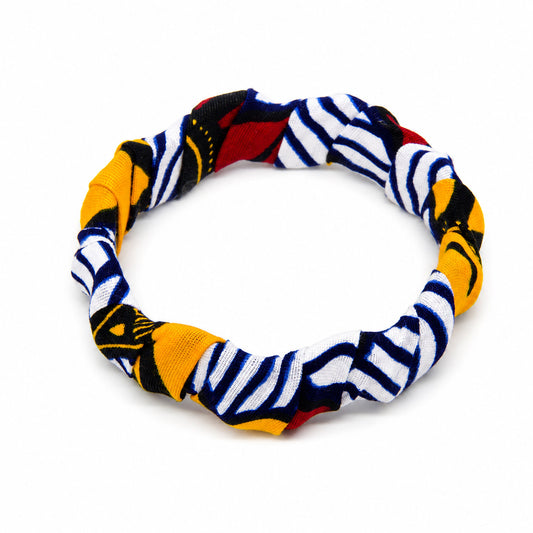 Bracelet jonc ondulé en bois recouvert de tissu wax blanc à rayures bleu marine, détails jaunes et rouges, isolé sur fond blanc.