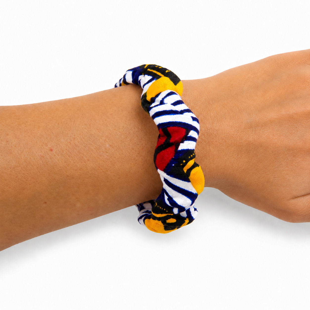 Bracelet jonc ondulé en bois recouvert de tissu wax blanc à rayures bleu marine, détails jaunes et rouges, porté au poignet sur fond blanc.