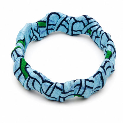 Bracelet jonc ondulé en bois recouvert de tissu wax bleu ciel aux motifs géométriques bleu marine et touches de vert, isolé sur fond blanc.