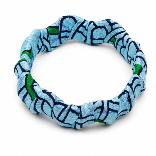 Bracelet jonc ondulé en bois recouvert de tissu wax bleu ciel aux motifs géométriques bleu marine et touches de vert, isolé sur fond blanc.