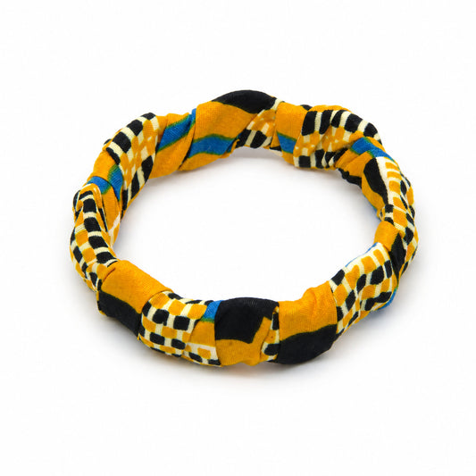 Bracelet jonc ondulé en bois recouvert de tissu wax jaune vibrant aux motifs géométriques complexes (damiers noirs, bandes bleu royal), isolé sur fond blanc pour vue produit.