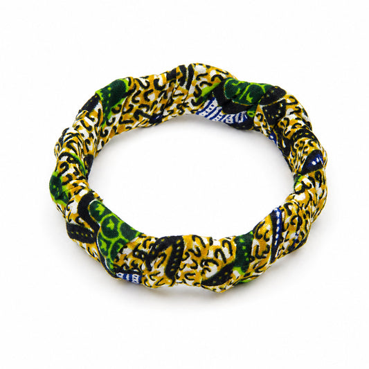 Bracelet jonc ondulé en bois recouvert de tissu wax jaune et vert aux motifs graphiques noirs, isolé sur fond blanc.