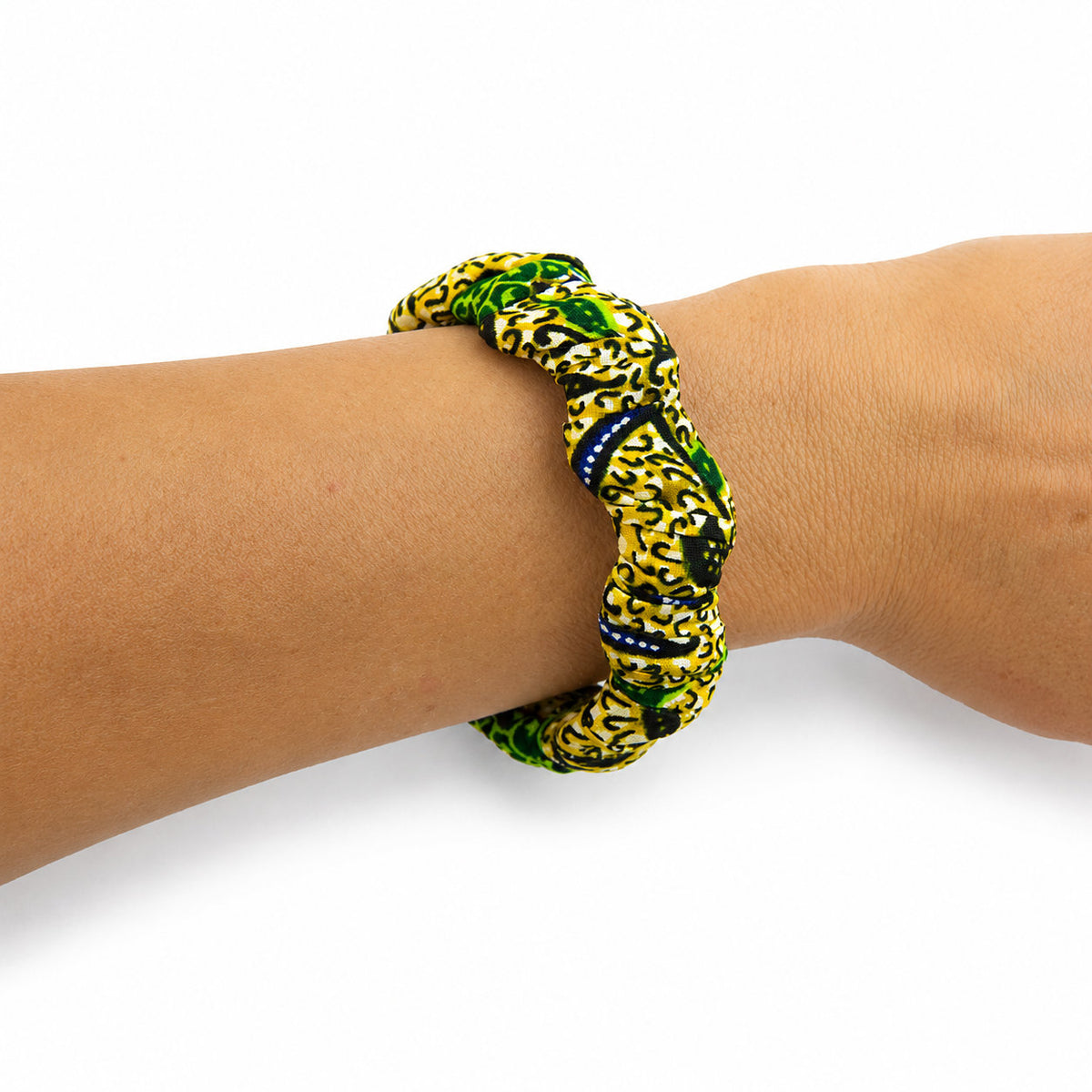 Bracelet jonc ondulé en bois recouvert de tissu wax jaune et vert aux motifs graphiques noirs, porté au poignet sur fond blanc.