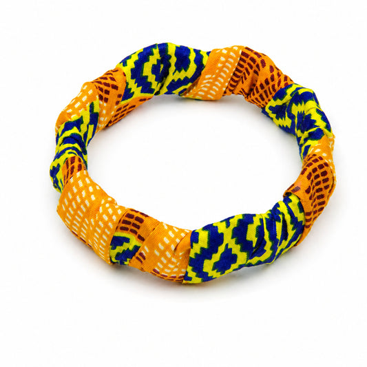 Bracelet jonc ondulé en bois recouvert de tissu wax aux motifs géométriques jaune-vert/bleu et texture orange/marron, isolé sur fond blanc.