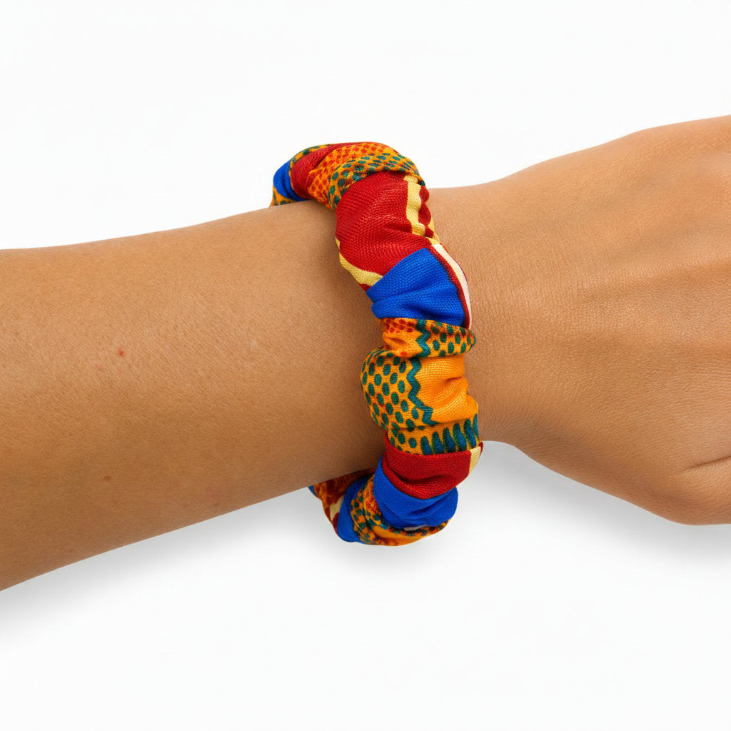Bracelet jonc ondulé en bois recouvert de tissu wax multicolore bleu royal, rouge et jaune, porté au poignet.