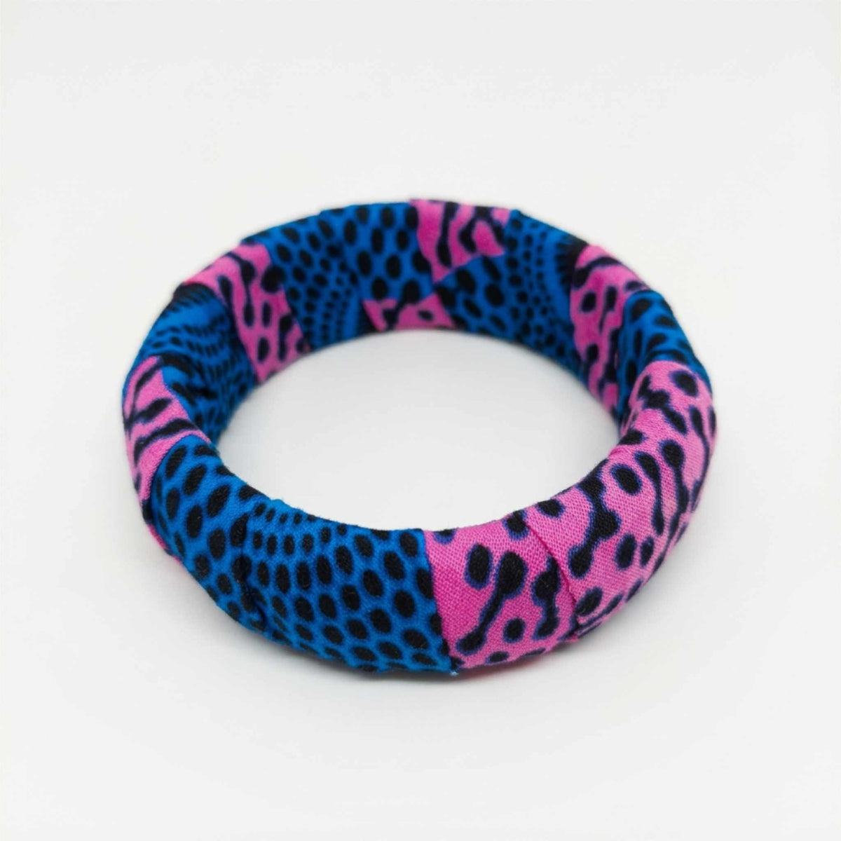 Bracelet jonc rigide habillé de tissu wax rose fuchsia et bleu intense à motifs tachetés.