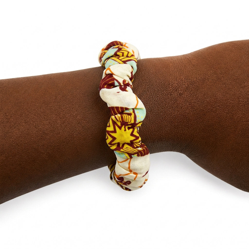 Bracelet en tissu wax jaune, bordeaux et bleu clair porté au poignet.