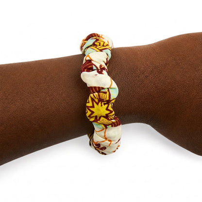 Bracelet en tissu wax jaune, bordeaux et bleu clair porté au poignet.