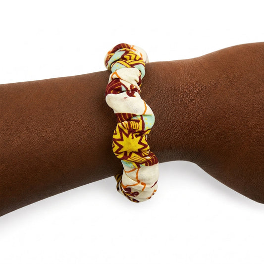Bracelet en tissu wax jaune, bordeaux et bleu clair porté au poignet.