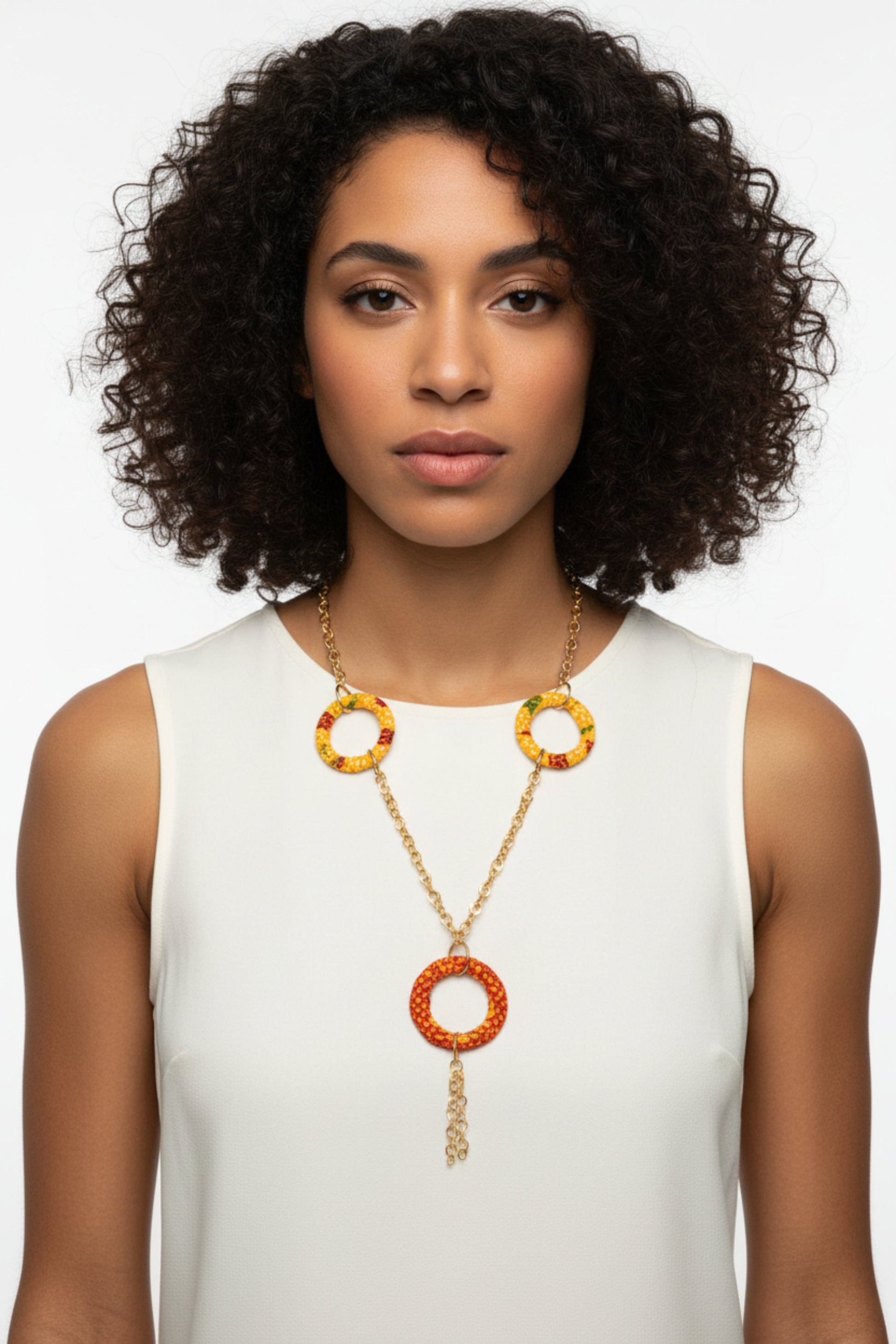 Femme portant un collier sautoir doré avec anneaux recouverts de tissu wax jaune orangée et grand anneau central orange rouge avec chaîne pendante - Bijou artisanal africain Djêkoo Wax
