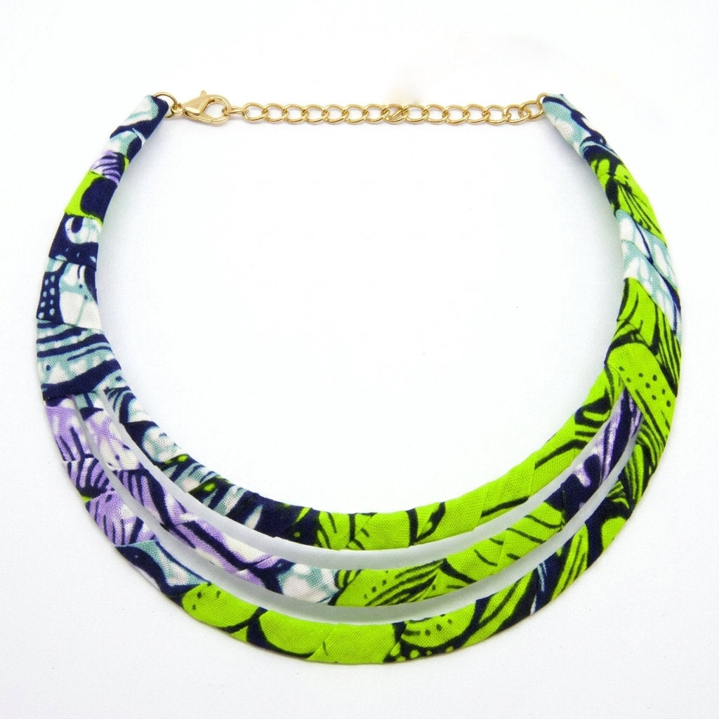 Collier ras de cou triple rang à plat sur fond blanc, confectionné en tissu wax aux motifs vert anis, violet et bleu marine, avec fermoir et chaînette dorés.