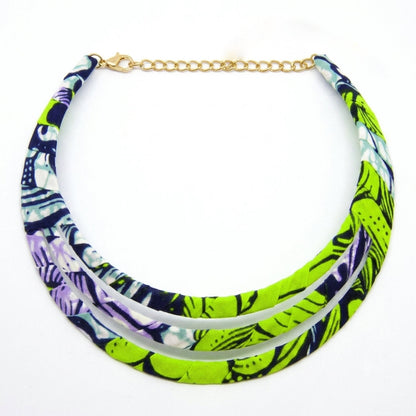 Collier ras de cou triple rang à plat sur fond blanc, confectionné en tissu wax aux motifs vert anis, violet et bleu marine, avec fermoir et chaînette dorés.
