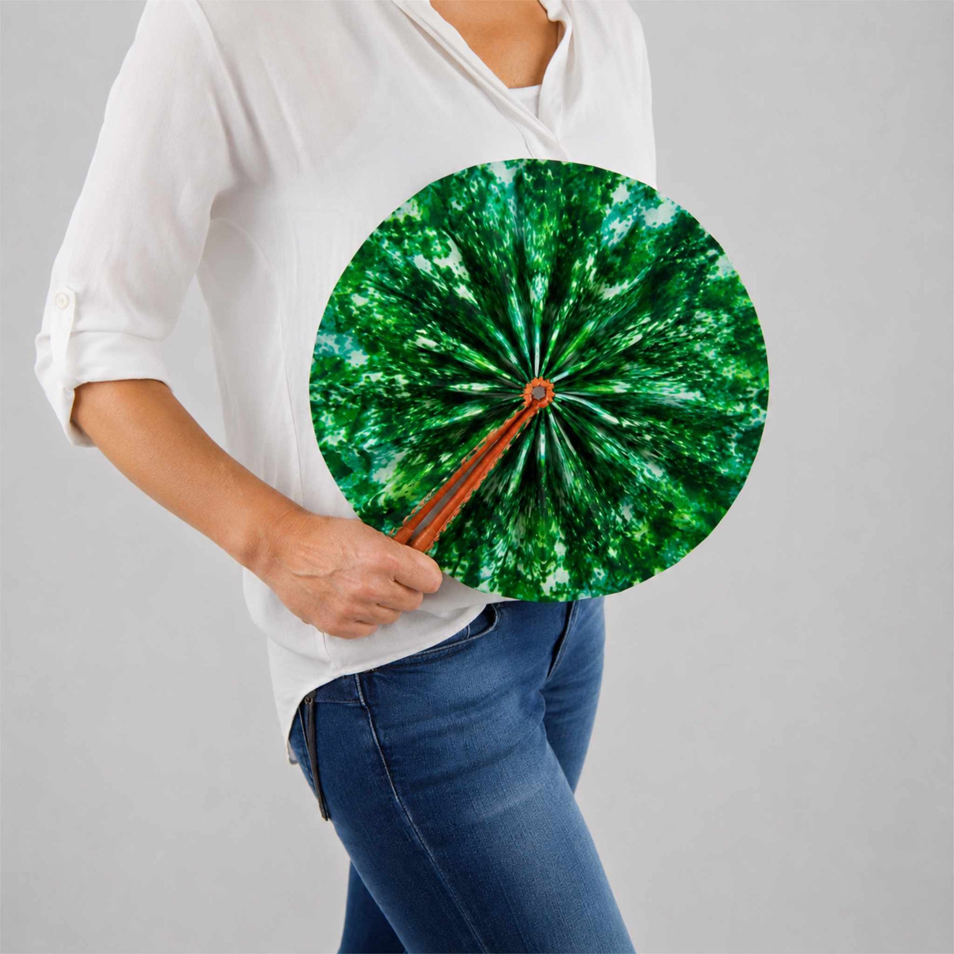 Éventail africain artisanal rond en tissu wax vert, présenté ouvert et tenu à la main avec une blouse blanche et un jean.