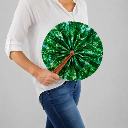 Éventail africain artisanal rond en tissu wax vert, présenté ouvert et tenu à la main avec une blouse blanche et un jean.