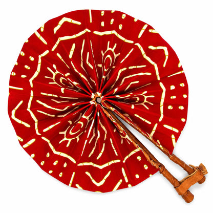 Éventail africain pliable rond en tissu wax rouge à motifs jaunes, avec manche en bois et finition en cuir, sur fond blanc.