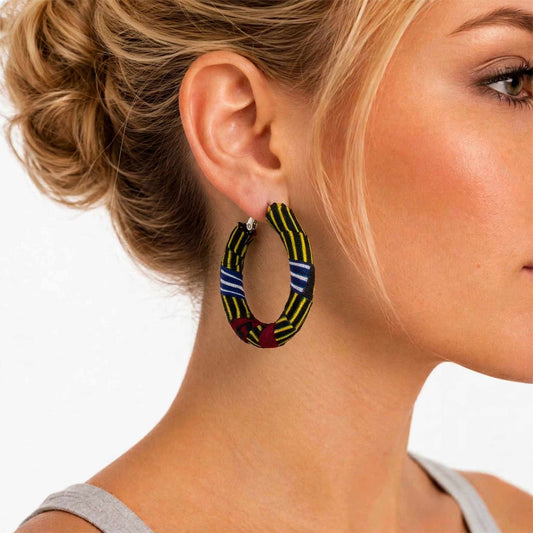 Gros plan de profil d'une femme portant une boucle d'oreille créole recouverte de tissu wax à rayures jaunes, bleues et rouges.
