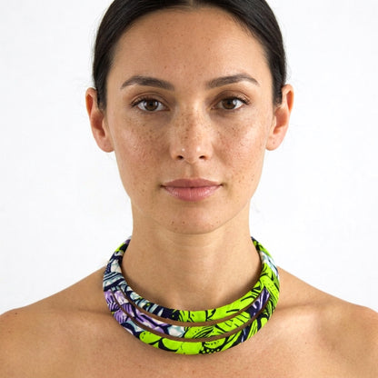 Portrait de face d'une femme portant le collier ras de cou triple rang en tissu wax vert anis et violet.