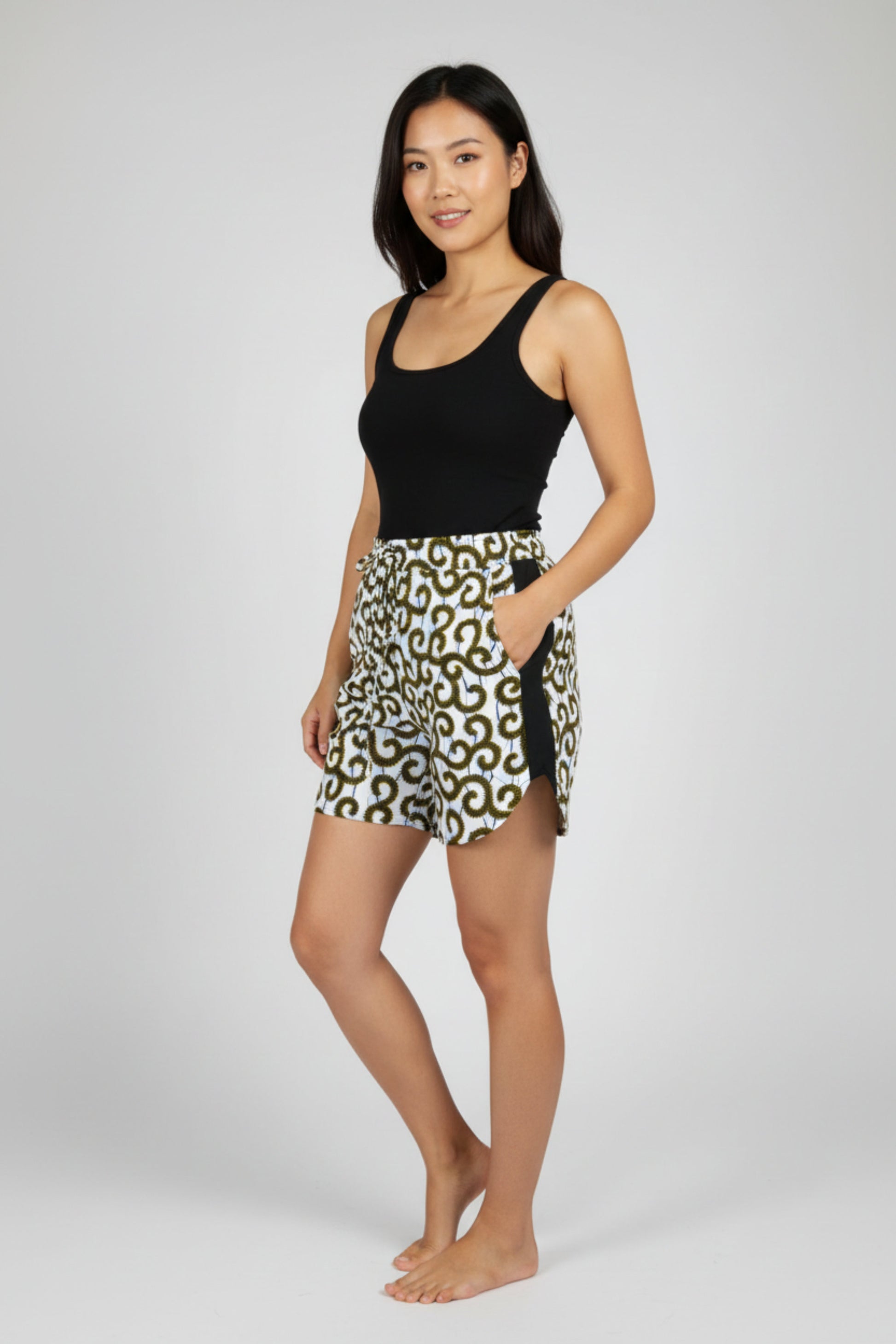 Femme portant un short en tissu wax blanc cassé à motifs spirales noir et jaune  avec ceinture élastique nœud noir et bandes latérales noires - Mode africaine femme Djêkoo Wax

