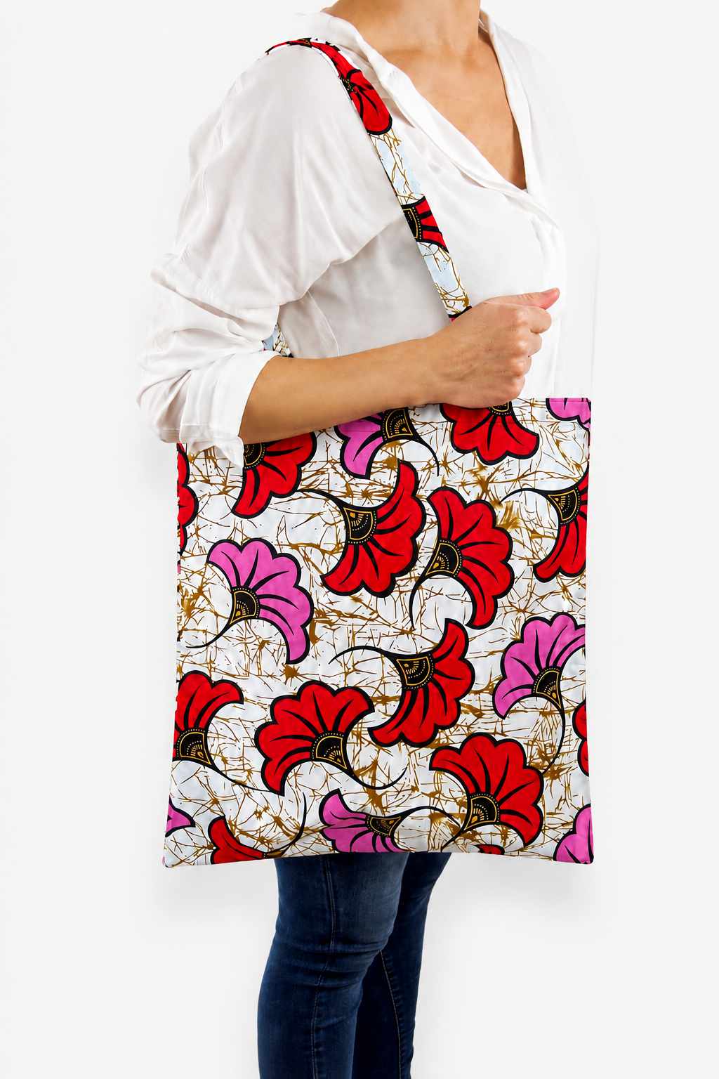 Tote bag artisanal fait main en tissu wax blanc à motif Fleurs de mariage rouge et rose, porté à l’épaule avec une tenue blanche
