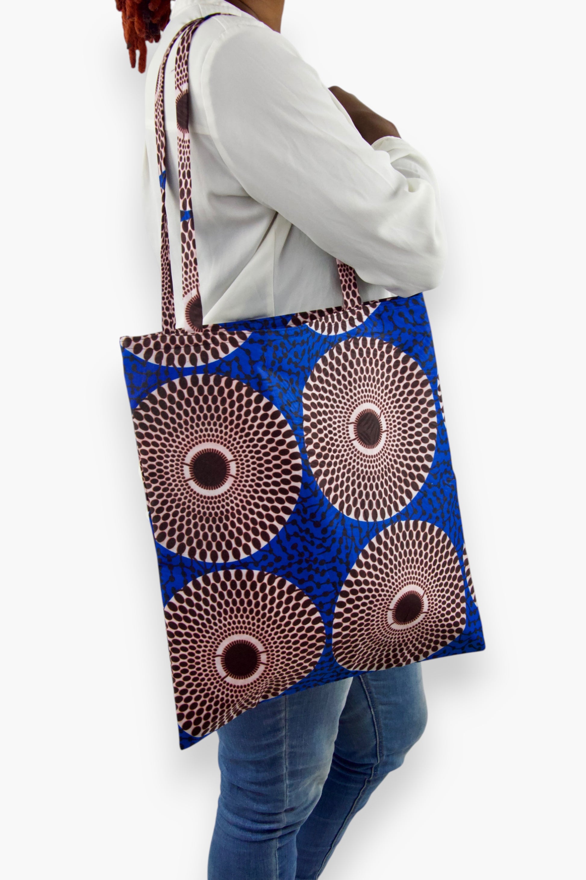Tote bag en tissu wax bleu royal, marron et blanc au motif Disque, présenté porté à l’épaule avec de longues anses assorties.